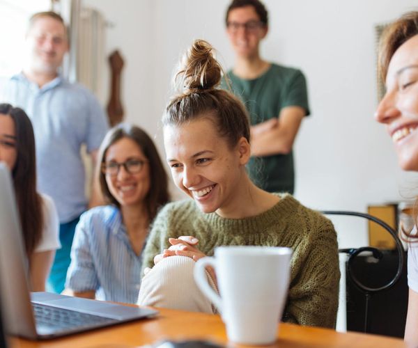 A diverse group of people smiling and looking relaxed in a bright room.